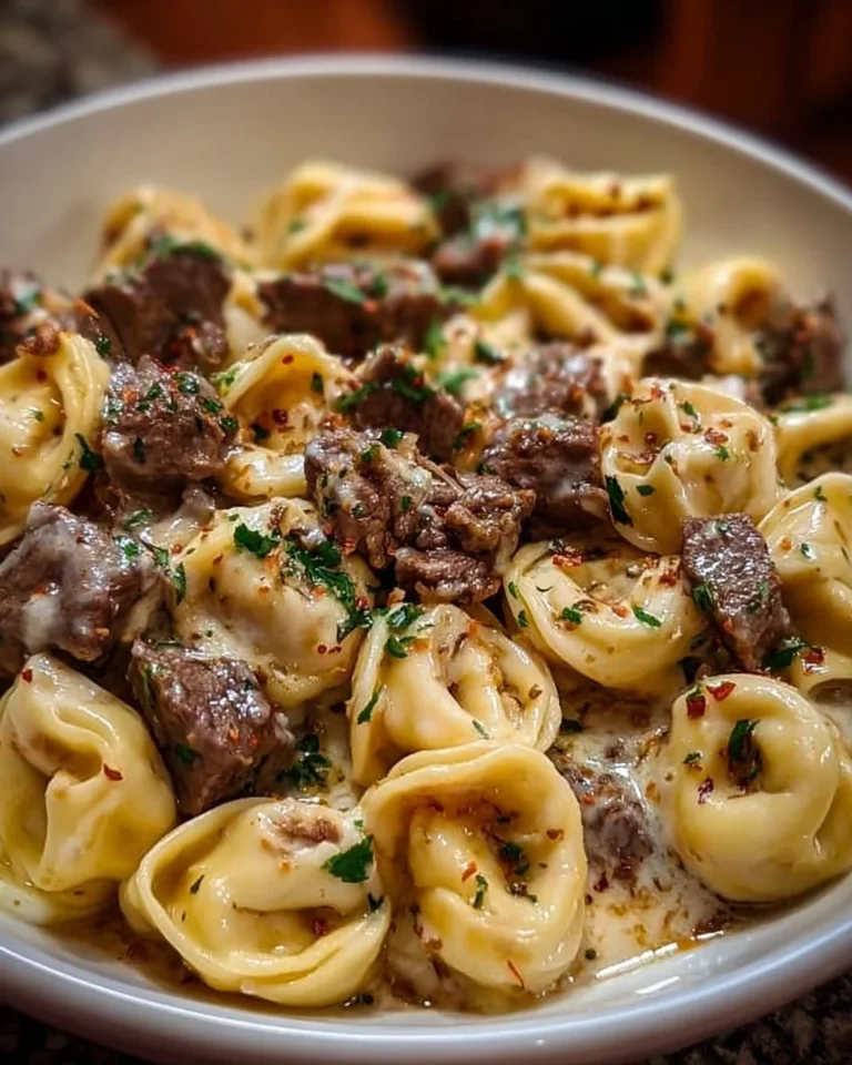 Plate of cheesesteak tortellini in rich provolone sauce with toppings.